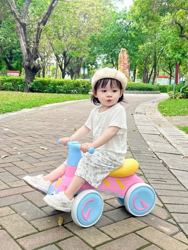 Bé ngồi xe chòi chân bốn bánh màu hồng ở công viên
