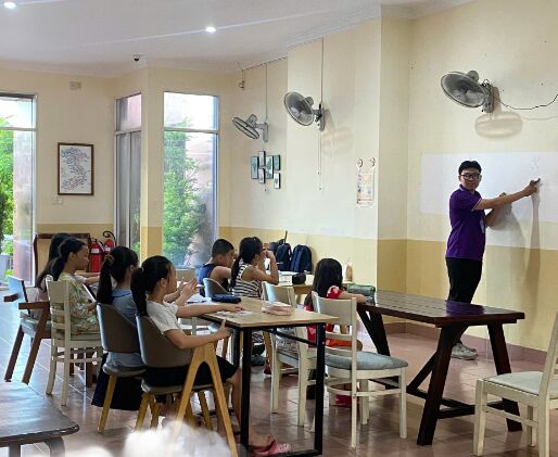 Gia sư kèm hai bạn nhỏ làm bài tại bàn