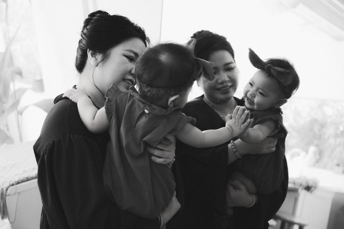 Hai người mẹ bế con, hai bé chạm tay nhau và cười