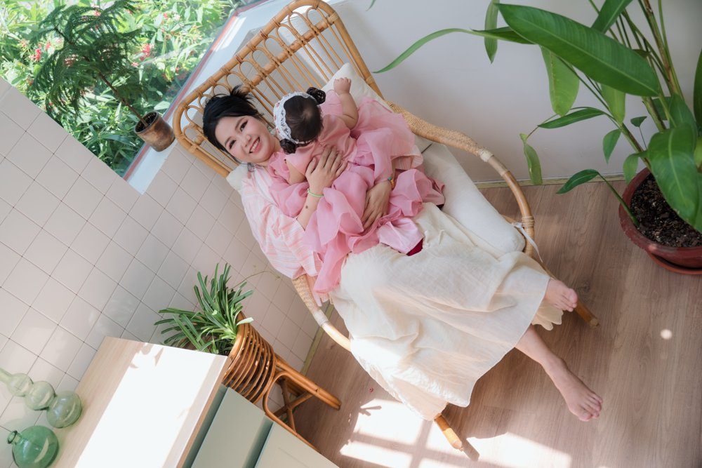 Chị Huệ ngồi ghế mây, ôm con gái nhỏ trong lòng