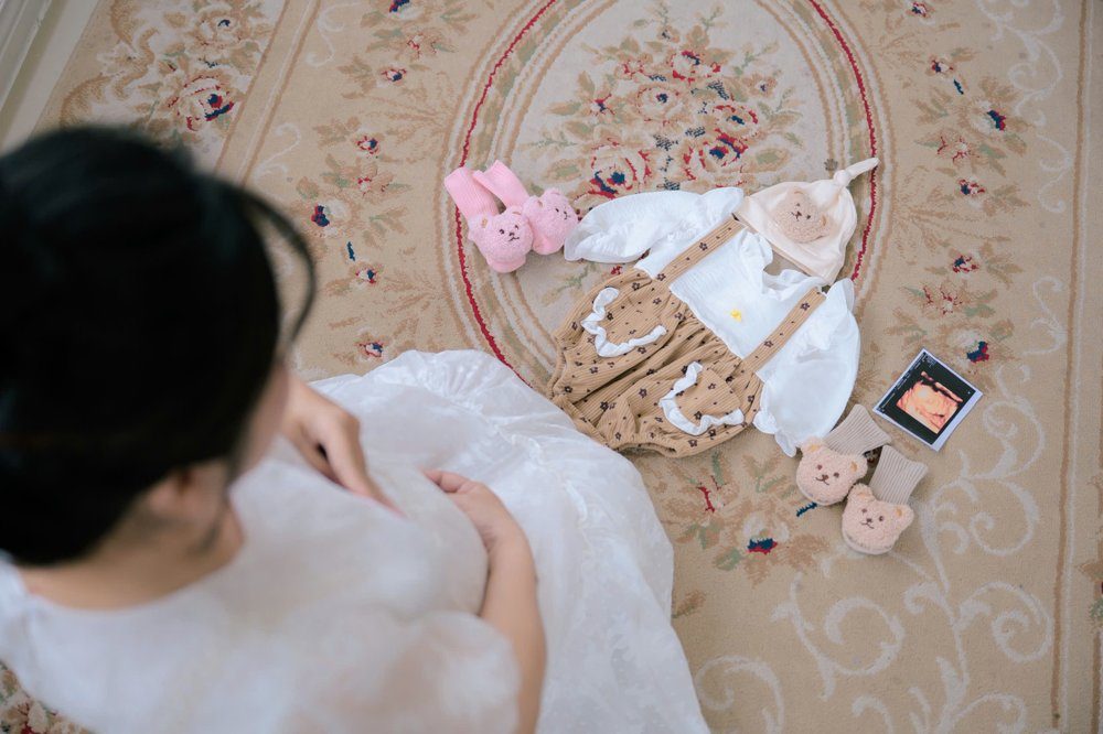 Chị Huệ khi mang thai, ngồi nhìn bộ đồ em bé, đôi tất và ảnh siêu âm bày trên thảm