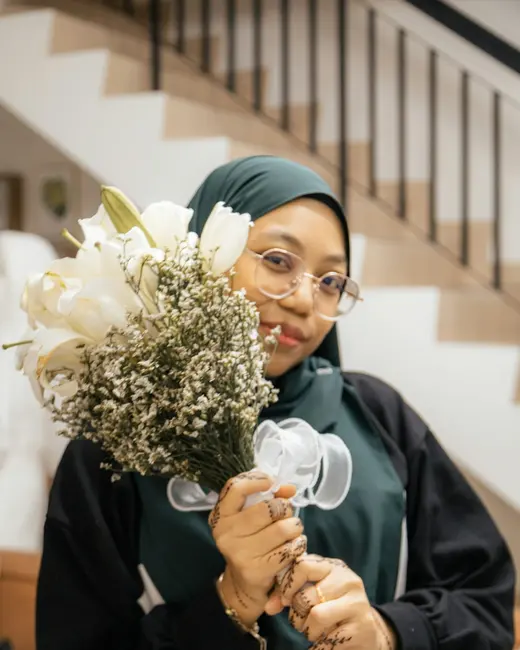 Wanita berhijab memegang jambangan bunga sebagai hadiah