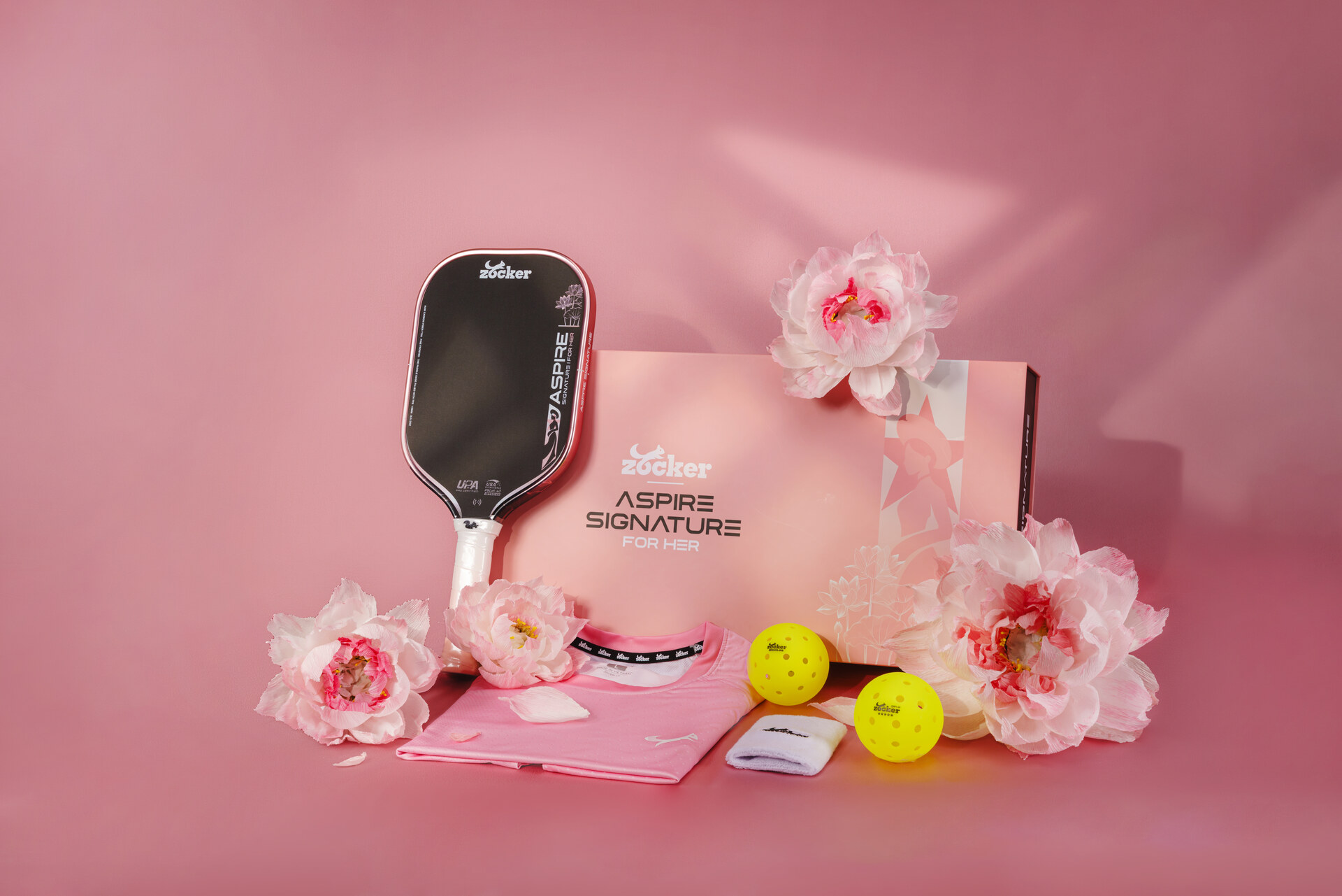 Set Aspire Signature: vợt, áo, băng chặn và hai bóng trên nền hoa hồng