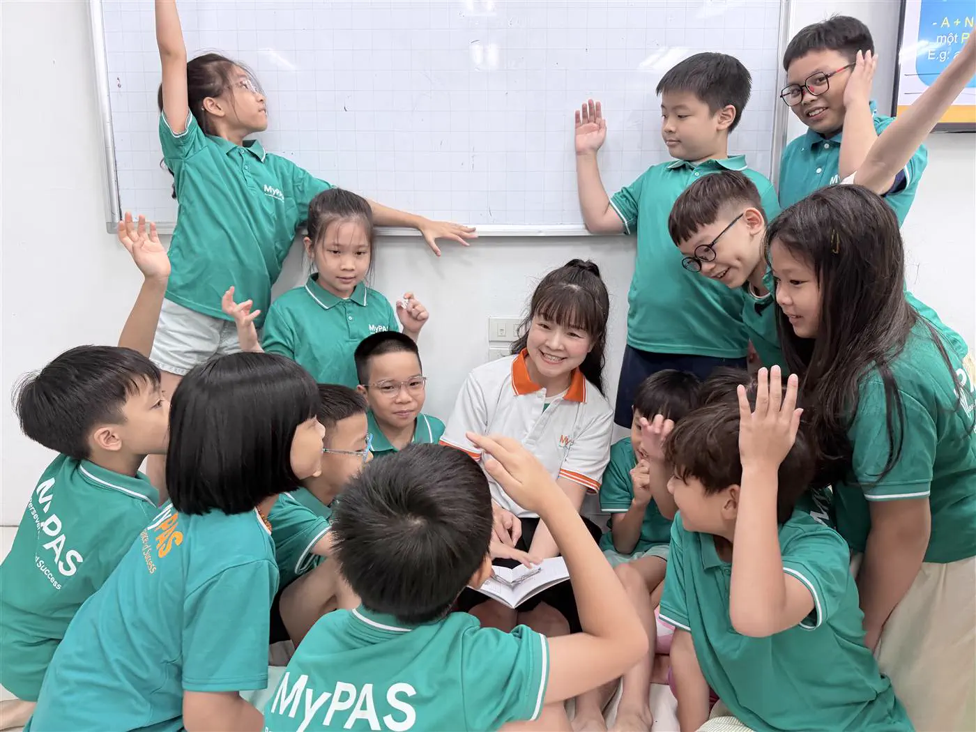 Cô giáo MyPAS ngồi giữa lớp, học sinh giơ tay phát biểu